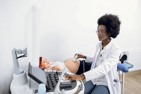 Молодая привлекательная профессионально привлекательная афроамериканка-врач делает 3-е УЗИ на животе беременной женщины в клинике. УЗИ для беременной женщины — стоковое фото