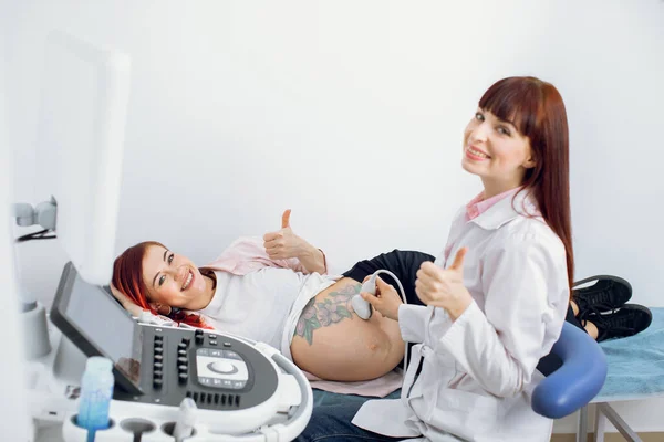 Prueba de detección profesional de la mujer embarazada por ultrasonido, sonriendo y mostrando el pulgar hacia arriba. Feliz alegre hipster embarazada mujer acostada en el sofá y mostrando el pulgar hacia arriba. —  Fotos de Stock
