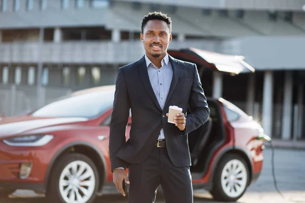 Uomo d'affari che beve caffè mentre carica auto — Foto Stock