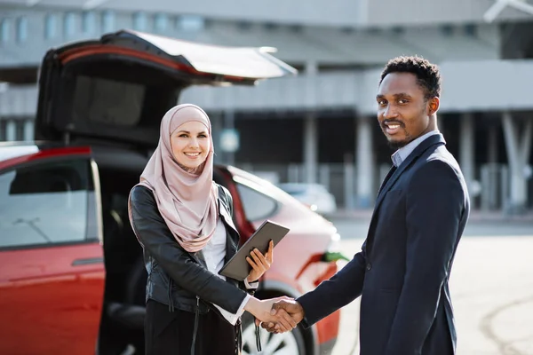 Femme musulmane vendant une voiture électrique à un homme d'affaires africain — Photo