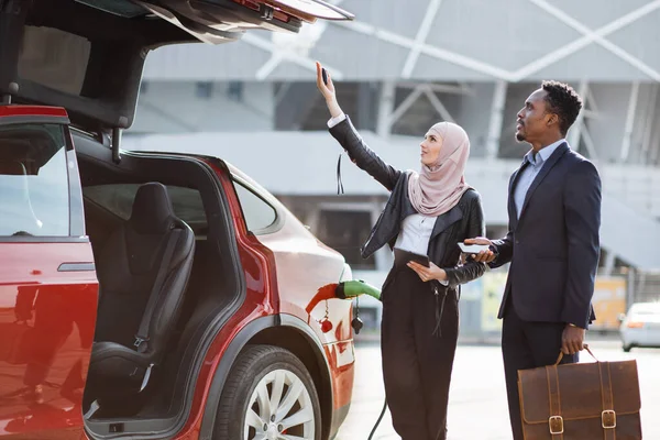 Γυναίκα με μαντίλα που παρουσιάζει ηλεκτρικό αυτοκίνητο στον αρσενικό πελάτη — Φωτογραφία Αρχείου