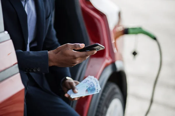 Mannen sitter i elbil med mobil och pengar kontanter — Stockfoto