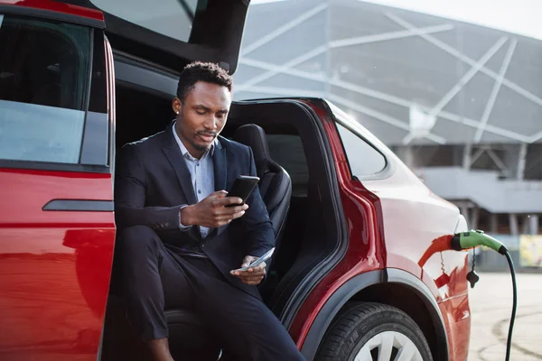 Homme assis en voiture électrique avec mobile et argent comptant — Photo