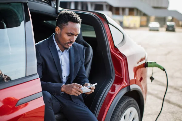 Mann mit Bargeld sitzt in aufladendem Elektroauto — Stockfoto