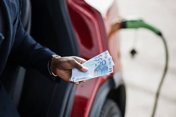 Uomo che detiene denaro contante per la ricarica di auto elettriche — Foto Stock