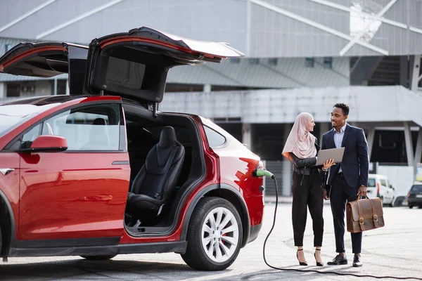 Uomo e donna che parlano mentre l'auto elettrica si ricarica — Foto Stock