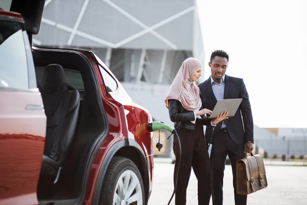 Vendeur utilisant un ordinateur portable tout en montrant la voiture électrique au client — Photo