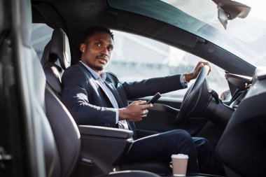 Afrikalı adam araba kullanıyor ve modern akıllı telefon kullanıyor.