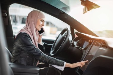 Arabada cep telefonuyla konuşan bir kadın gösterge paneline dokunuyor