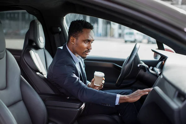 African man sitting in modern car and using dashboard