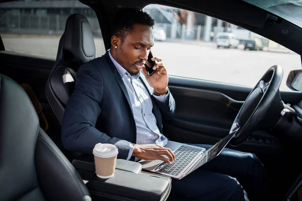 Επιχειρηματίας μιλώντας στο κινητό και πληκτρολογώντας σε φορητό υπολογιστή στο αυτοκίνητο — Φωτογραφία Αρχείου