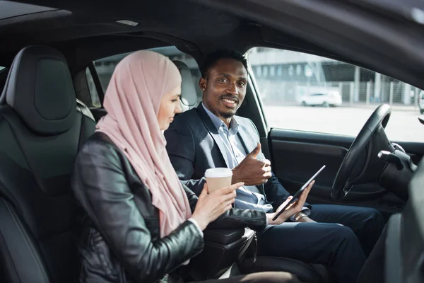 Man i kostym och kvinna i hijab med mobiltelefon i bilen — Stockfoto