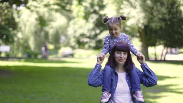 Schattige kleine 3-jarige dochter op een piggy back ride met haar charmante moeder, wandelen in prachtige stad zomer park. gelukkig meisje en mam lachen en genieten samen tijdens wandelen in park. — Stockvideo