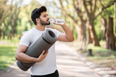 Spor elbiseli Arap adam şişeden su içiyor.