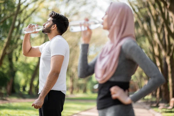 Muslim couple in sport outfit drinking water outdoors