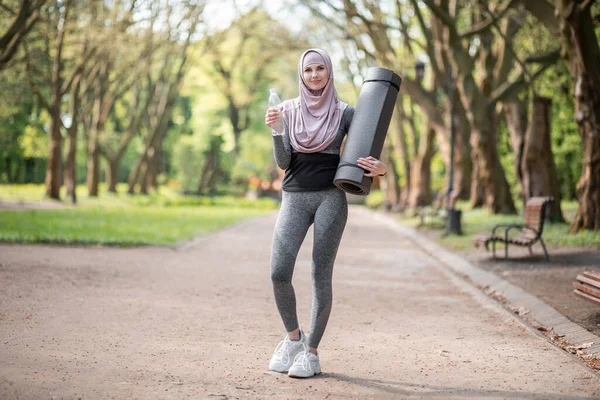 Mujer musulmana con esterilla de yoga bebiendo agua después del entrenamiento — Foto de Stock
