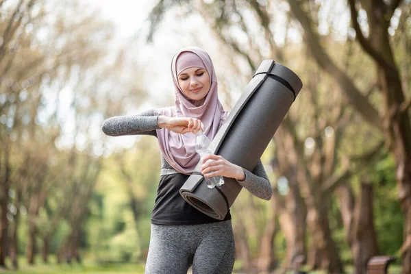 Muslim woman in sport outfit drinking water after workout