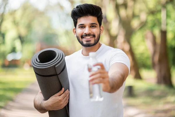 Homem de roupas esportivas posando no parque com garrafa de água — Fotografia de Stock