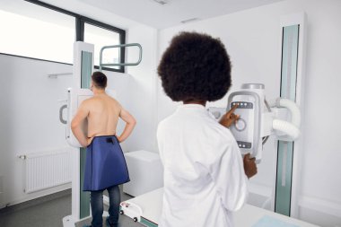 Kadın doktor radyoloji uzmanı göğüs taraması yapıyor. Genç beyaz adamın hastanede röntgeni çekiliyor. Florografi ve göğüs muayenesi kavramı.