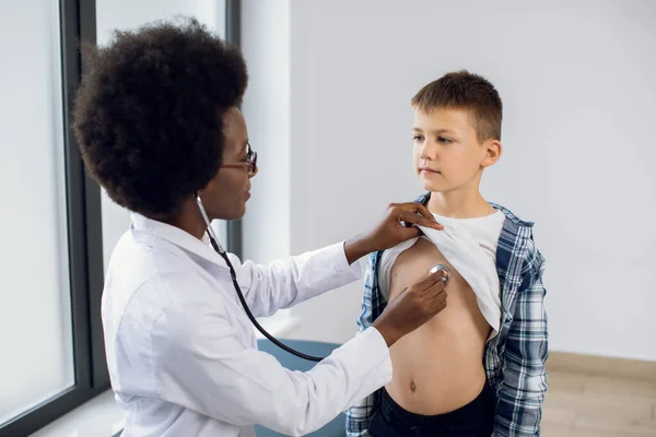 Steteskopu olan Afrikalı kadın bir pediatrist. Beyaz bir erkek hasta. Siyah hekim, kalp atışlarını ve ciğerlerini kontrol eder. Çocuğun solunumunu kontrol eder. Aşıdan önce kontrol eder..