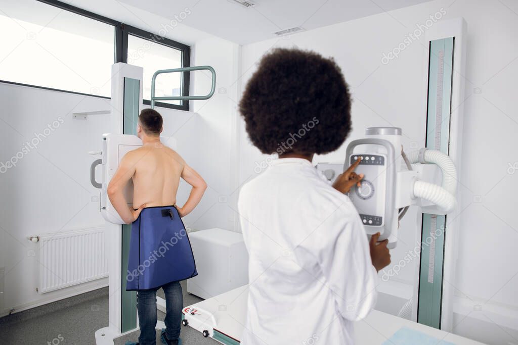 Back view of female doctor radiologist taking chest scan Xray of young Caucasian man in hospital. Fluorography and chest examination concept.