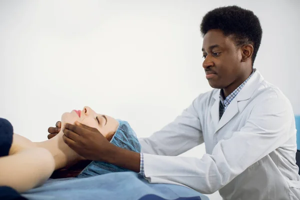 Massaggiatore uomo afroamericano che conduce un trattamento anti-invecchiamento massaggio facciale per giovane cliente femminile — Foto Stock