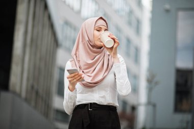 Arap iş kadını kahve içiyor ve akıllı telefon kullanıyor.