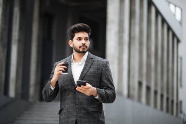 Akıllı telefon kullanan ve sokakta kahve içen Arap bir adam.