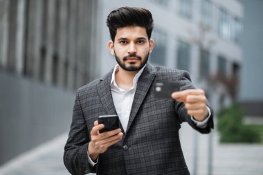 Arap işadamı dışarıda banka kartı ile cep telefonu kullanıyor.