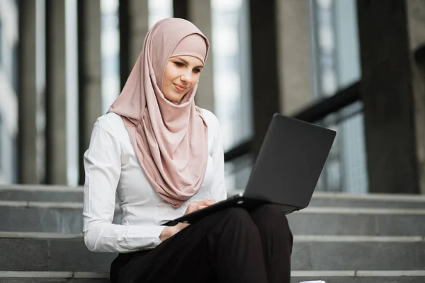 Sonriente joven en hijab woking en el ordenador portátil al aire libre — Foto de Stock