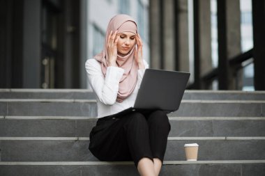 Laptoplu kadın dışarıda baş ağrısı çekiyor.
