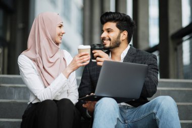 Müslüman iş arkadaşları açık havada kahve fincanlarıyla kadeh kaldırıyorlar.