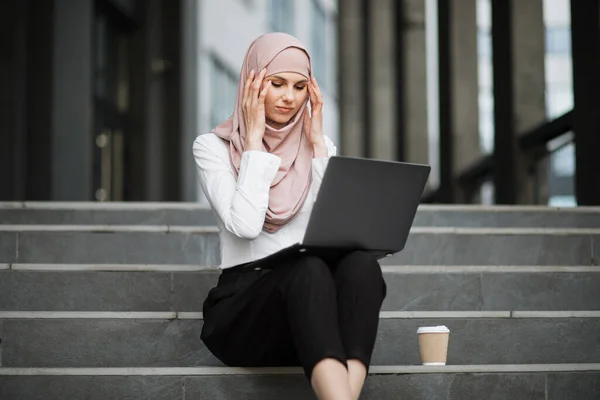 Жінка в хіджабі з ноутбуком страждає від головного болю на відкритому повітрі — стокове фото