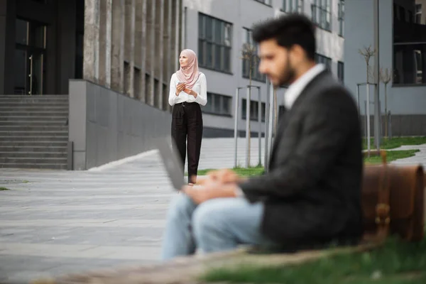 Muslimischer Mann arbeitet am Laptop, während Frau Smartphone nutzt — Stockfoto