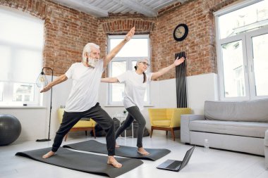 İki yaşlı insan yoga yaparken evde poz veriyor.