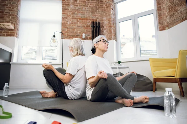 Mature couple sitting back to back and meditating at home — Stockfoto