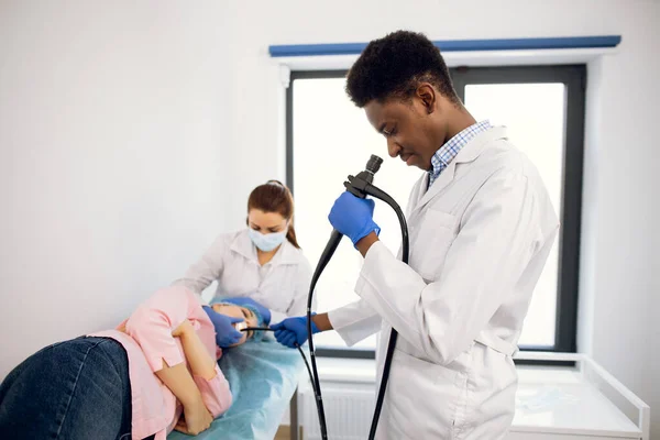 Jovem médico afro-americano segura um endoscópio, inserindo câmera na boca de paciente do sexo feminino — Fotografia de Stock