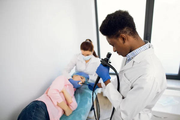 Médico afro-americano masculino com endoscópio e colega enfermeira examinando paciente jovem — Fotografia de Stock
