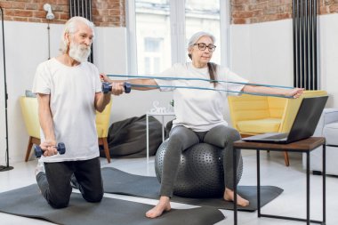 Yetişkin çift spor aletleriyle çalışırken dizüstü bilgisayar kullanıyor