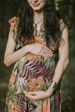 Hamile kadın parkta, zevkle bebek bekliyor ve karnına dokunuyor.