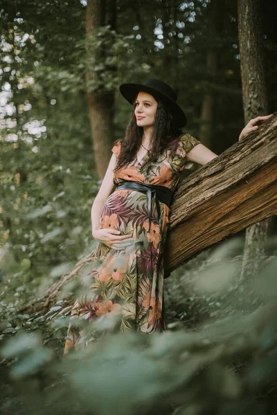 Mulher grávida muito jovem posando na floresta ou parque inclinado em uma árvore — Fotografia de Stock