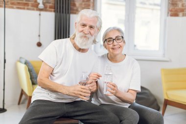 Olgun erkek ve kadın ev içi egzersizlerden sonra su içiyor.