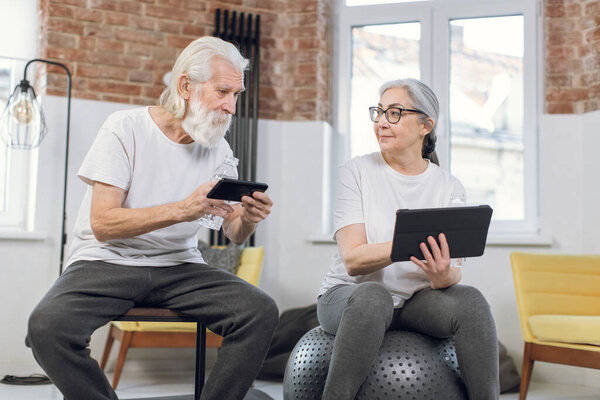 Senior couple resting after training with gadgets in hands