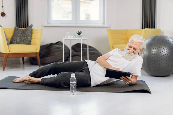 Hombre mayor acostado en esterilla de yoga y usando tableta digital —  Fotos de Stock