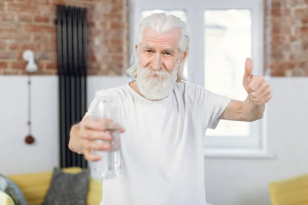 Idősebb férfi felemeli a hüvelykujját és egy üveg vizet tart a kezében. — Stock Fotó
