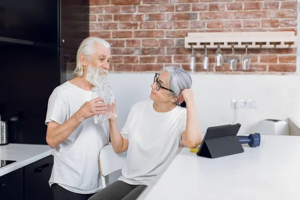 Θετικό ηλικιωμένο ζευγάρι πόσιμο νερό μετά την προπόνηση στο σπίτι — Φωτογραφία Αρχείου