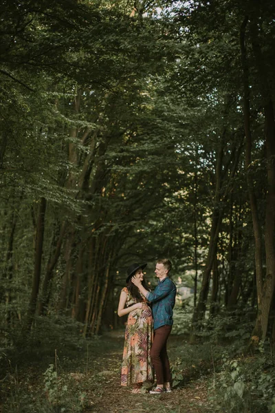 Heureux jeune homme touche son visage de femmes enceintes alors qu'ils se tiennent sur le chemin dans la forêt d'été. — Photo