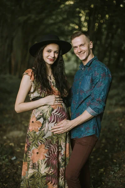 Jeune homme et sa femme enceinte attrayant, posant à la caméra dans la forêt — Photo