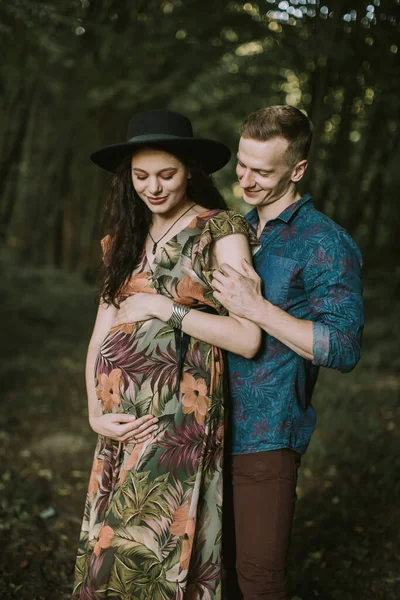 Привлекательная беременная женщина держит животик, красивый мужчина обнимает ее сзади — стоковое фото