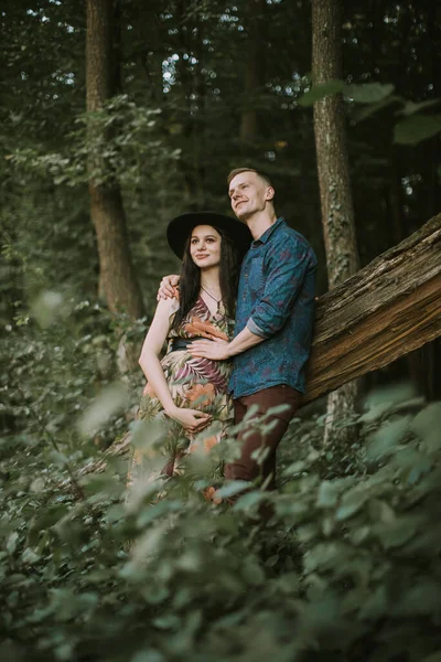 Беременная девушка с большим симпатичным животом и молодой человек в красивом лесу — стоковое фото